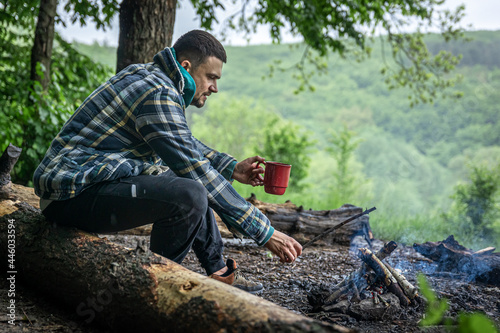A man on a hike sits by the fire and warms himself.