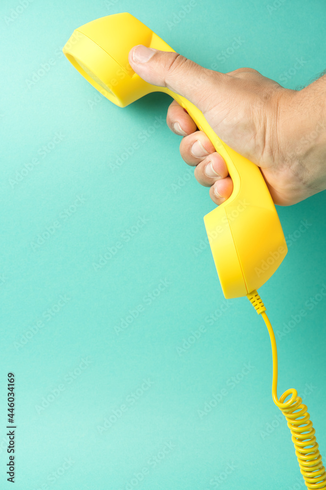 Retro yellow telephone receiver held by a hand on a turquoise blue background, space for text. Retro yellow telephone receiver held by a hand on a turquoise blue background, space for text.