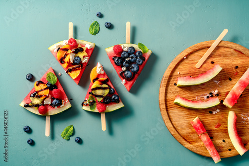 Watermelon pizza bar on blue table. Watermelon with assorti of berries, fruits and ricotta cheese. Pieces of watermelon with kiwi, blueberries, raspberries, apricots and orange on wooden board photo