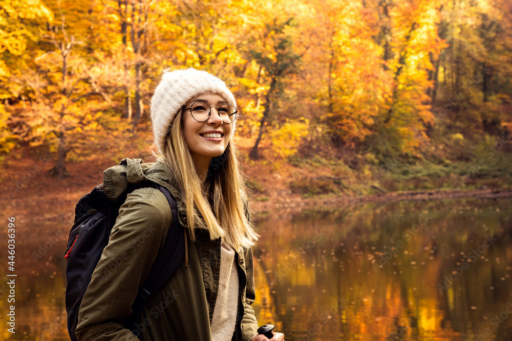 Portrait of young female hiker with backpack standing in forest by the lake.