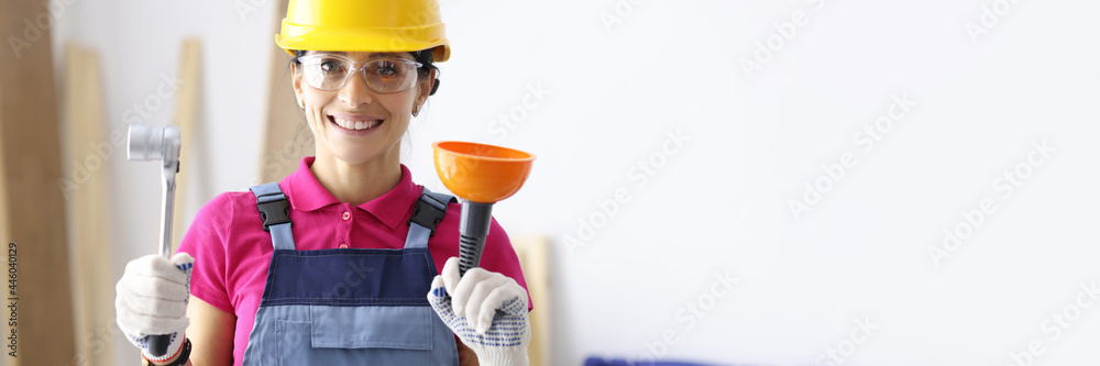 Woman in protective helmet holding plunger and wrench Woman in protective helmet holding plunger and wrench
