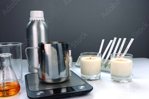 wax pouring pitcher is on the digital scales  on white table with fragrance  essential oil bottles and candles during the blending scent for making perfume and candle by the perfumer in the laboratory