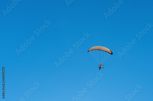 A powered paraglider trike flying over clear blue sky back view