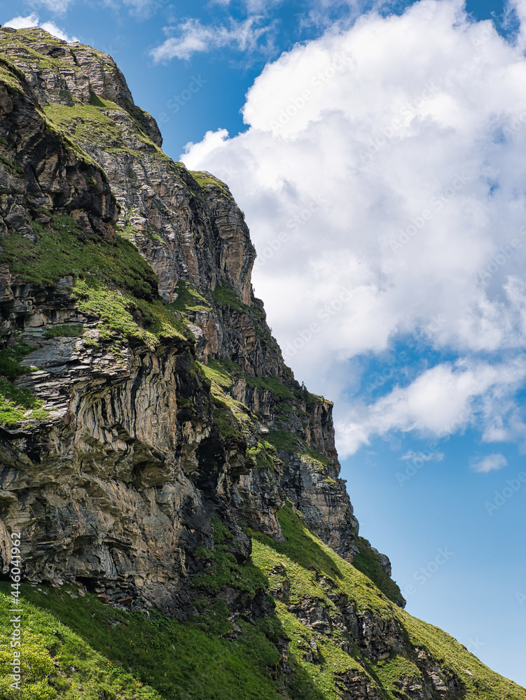 In Swiss Alps, rock wall with grass against blue sky with clouds