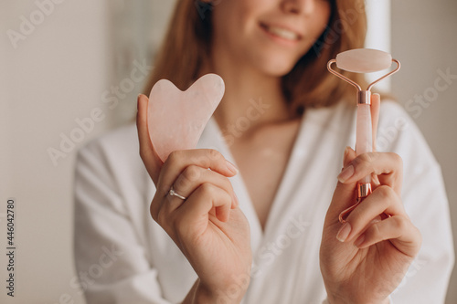Woman making massage with gua sha stone and face roller photo