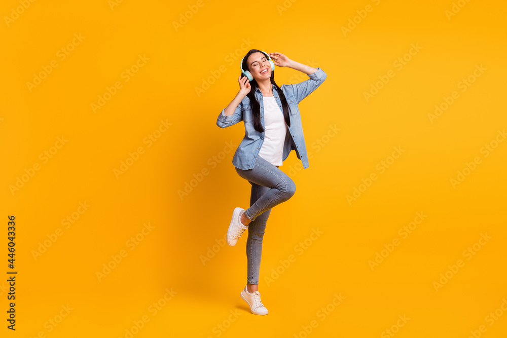 Full size photo of cool optimistic brunette lady listen music wear blue shirt jeans sneakers isolated on yellow color background