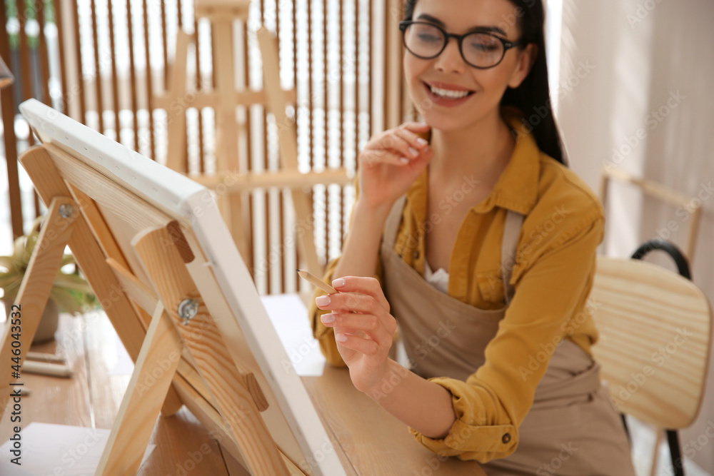 Young woman drawing on easel with pencil at table indoors Young woman drawing on easel with pencil at table indoors