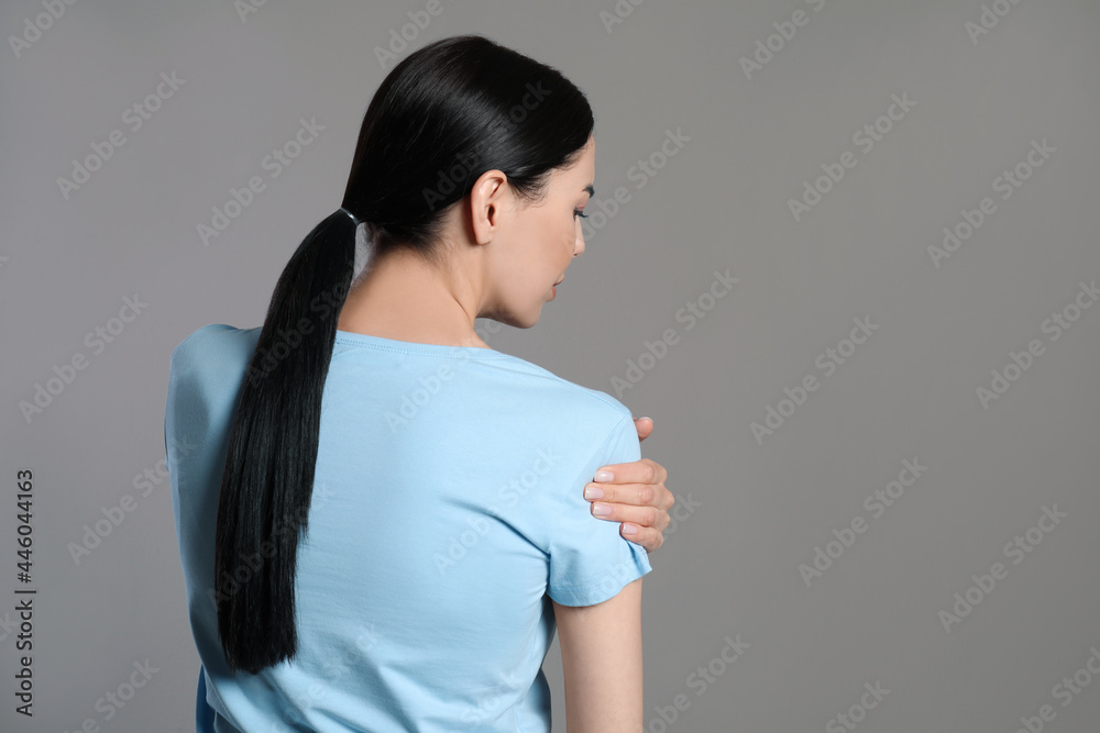Woman suffering from shoulder pain on beige background, back view Woman suffering from shoulder pain on beige background, back view
