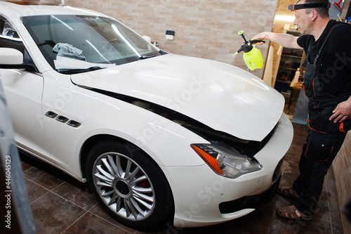 Worker in detailing garage put polyurethane anti-gravel film cover in white luxury car.