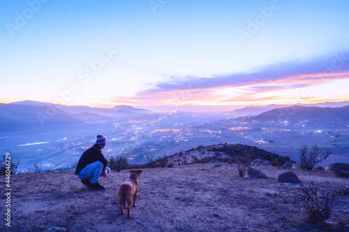 man and his dog staring at the sunset over the city on the mountain © oscargutzo