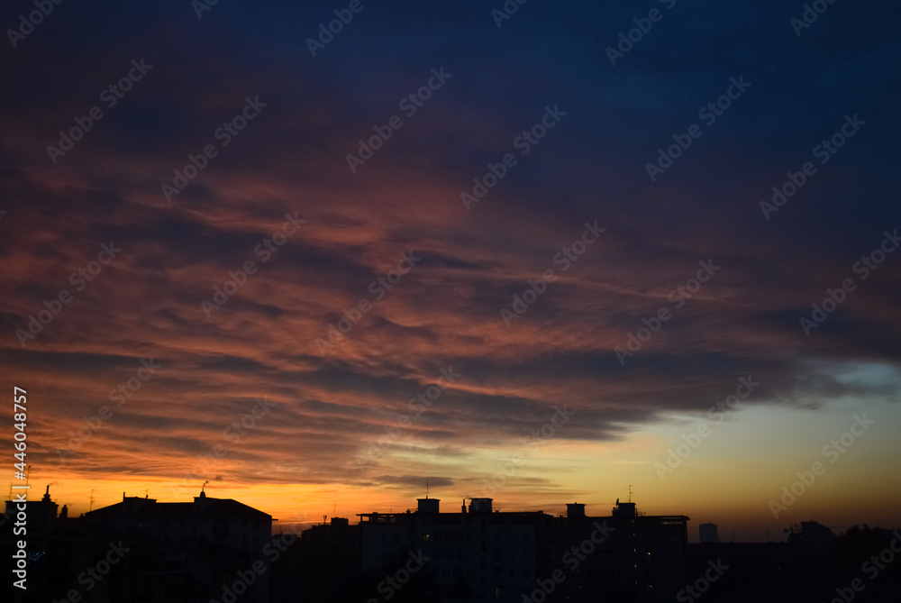 Dramatic orange clouds at sunset with city buildings silhouettes