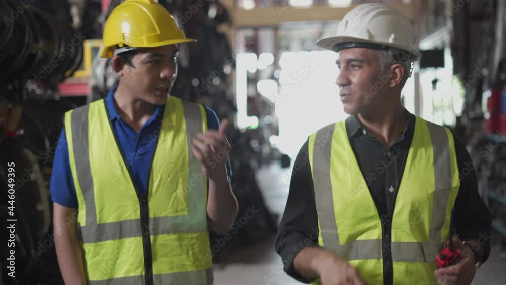 senior engineer talking with young asian worker while walking in old used car engine auto parts shop warehouse. manager Speak through walkie talkie in Recycle motor factory senior engineer talking with young asian worker while walking in old used car engine auto parts shop warehouse. manager Speak through walkie talkie in Recycle motor factory