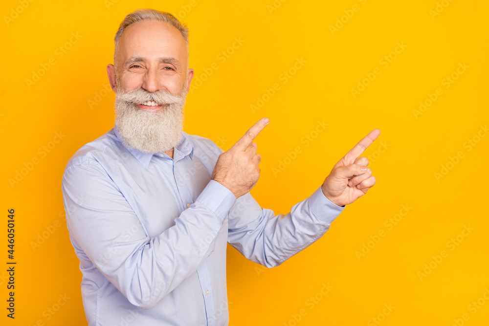 Photo of confident charming age gentleman wear blue shirt pointing two fingers empty space isolated yellow color background Photo of confident charming age gentleman wear blue shirt pointing two fingers empty space isolated yellow color background