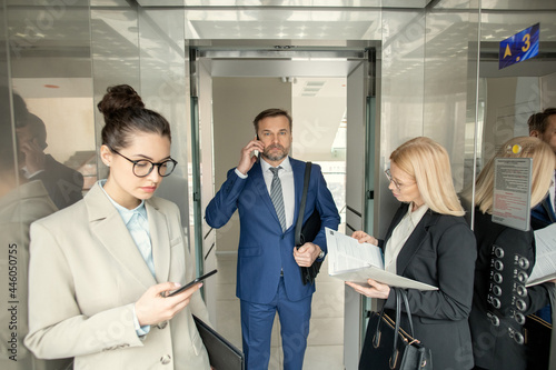Businessman in suit talking on mobile phone while going into the elevator with other people standing in it