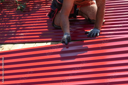 A man screws sheets of corrugated board on the roof with a screwdriver. Repair and replacement of the roof. Laying of corrugated sheets