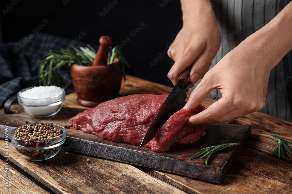 Woman cutting fresh raw meat at wooden table, closeup
