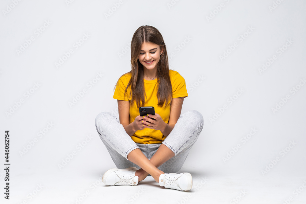 Woman sitting on floor and text messaging on a mobile phone isolated over white background Woman sitting on floor and text messaging on a mobile phone isolated over white background