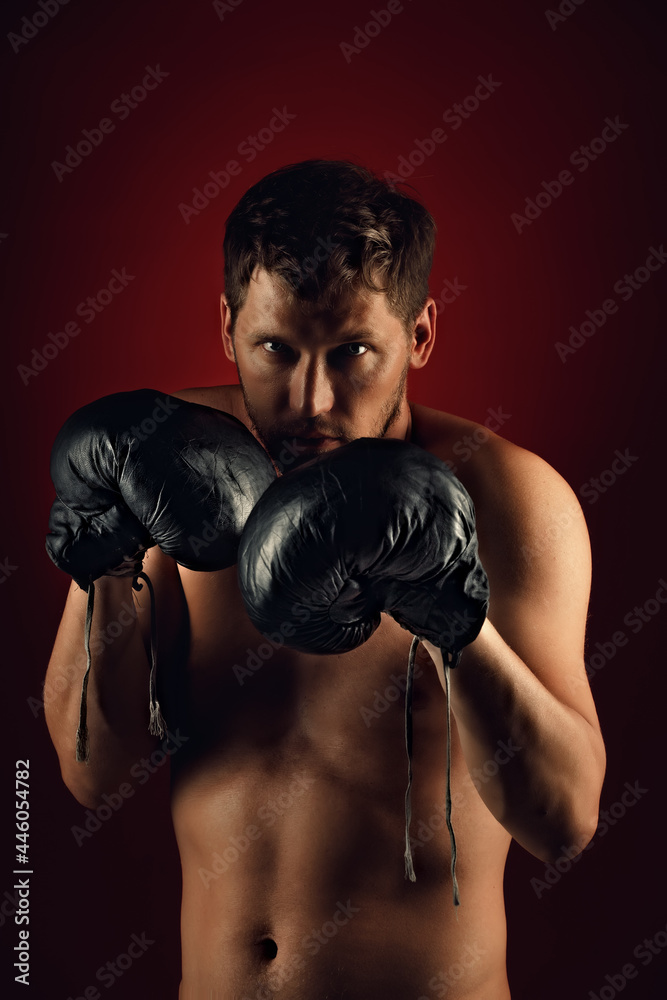 This is a dramatic portrait of a boxer in old boxing gloves on a dark background. An athletic mixed martial arts fighter stands in a fighting stance. Banner for sports events.