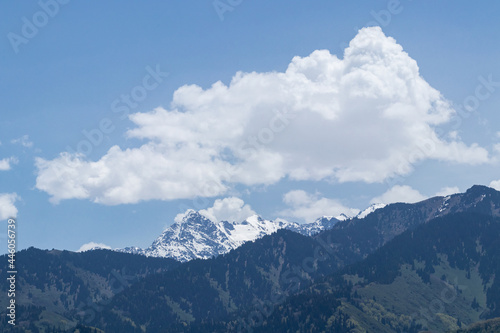 A snowy mountain peak behind the hills and white clouds above it