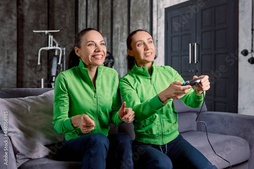 Joystick from game console in hands of woman who plays with support of her sister.