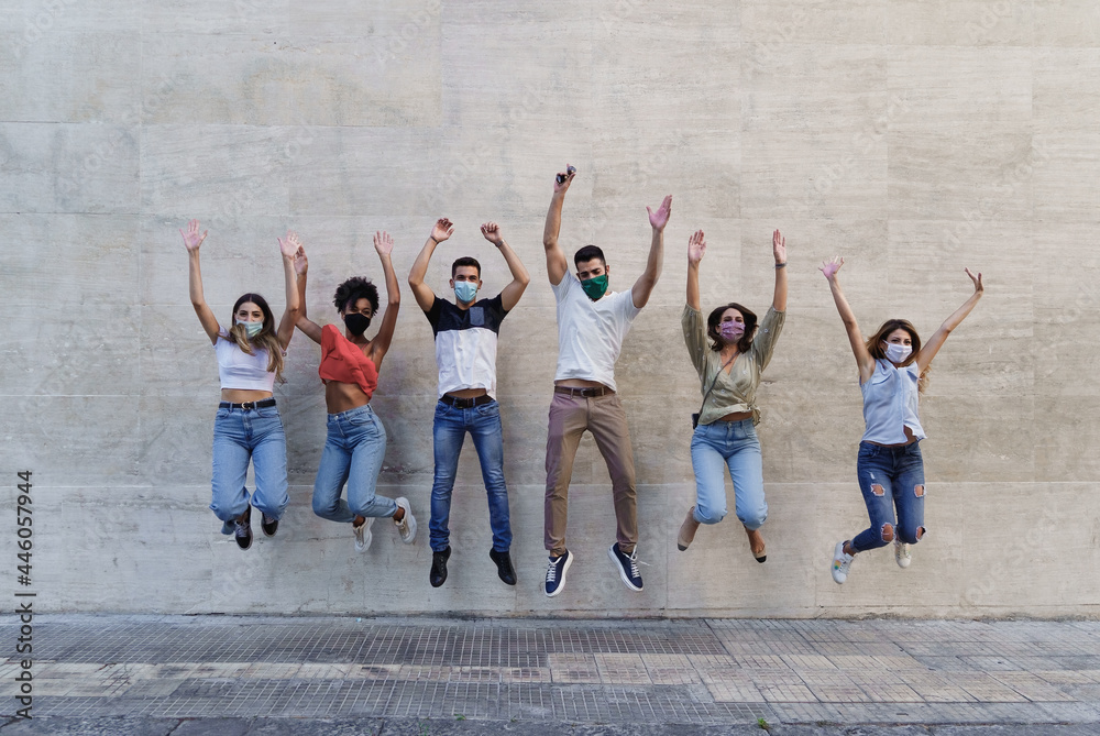 Obraz premium Young people with face masks jumping happy against a wall