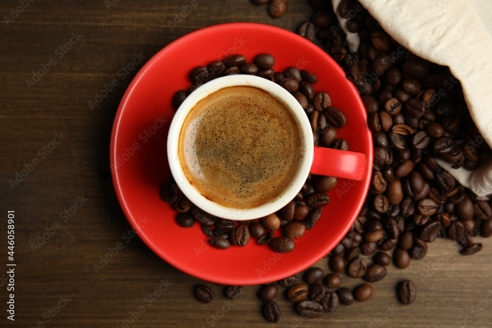 Obraz premium Cup of tasty coffee and beans on wooden table, flat lay