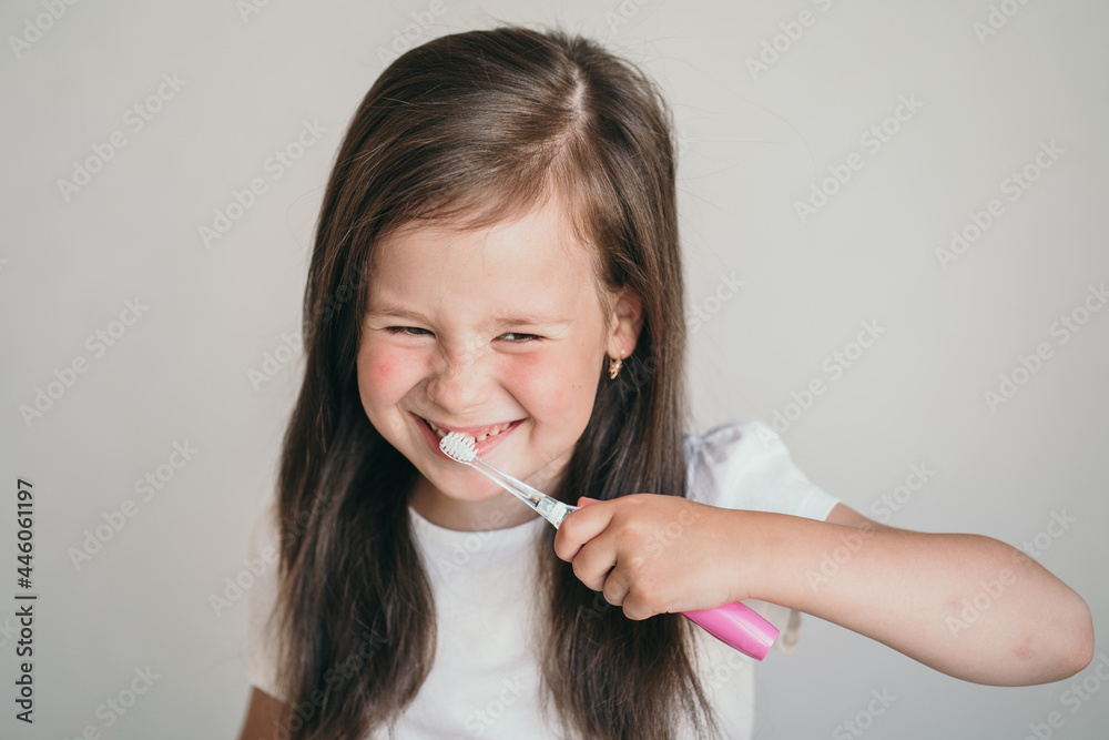 The child brushes his teeth with a brush. The little girl happily washes herself and takes care of her teeth. Pink toothbrush. Oral hygiene in children. The child brushes his teeth with a brush. The little girl happily washes herself and takes care of her teeth. Pink toothbrush. Oral hygiene in children.
