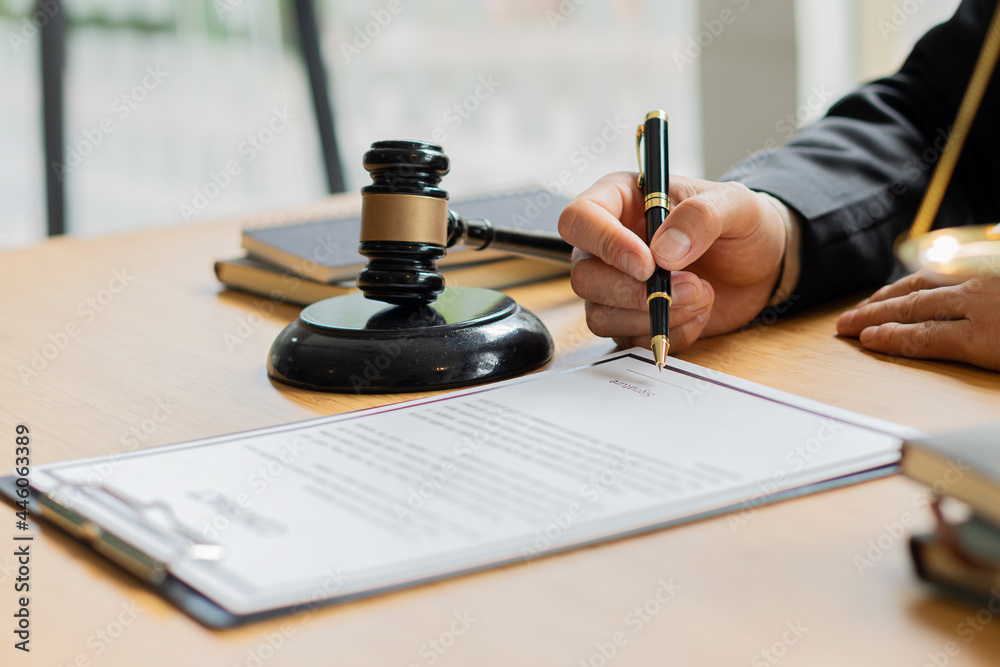 A lawyer working in an office and a judge's hammer and gold scales in front with a notebook on a legal advisor concept table. A lawyer working in an office and a judge's hammer and gold scales in front with a notebook on a legal advisor concept table.