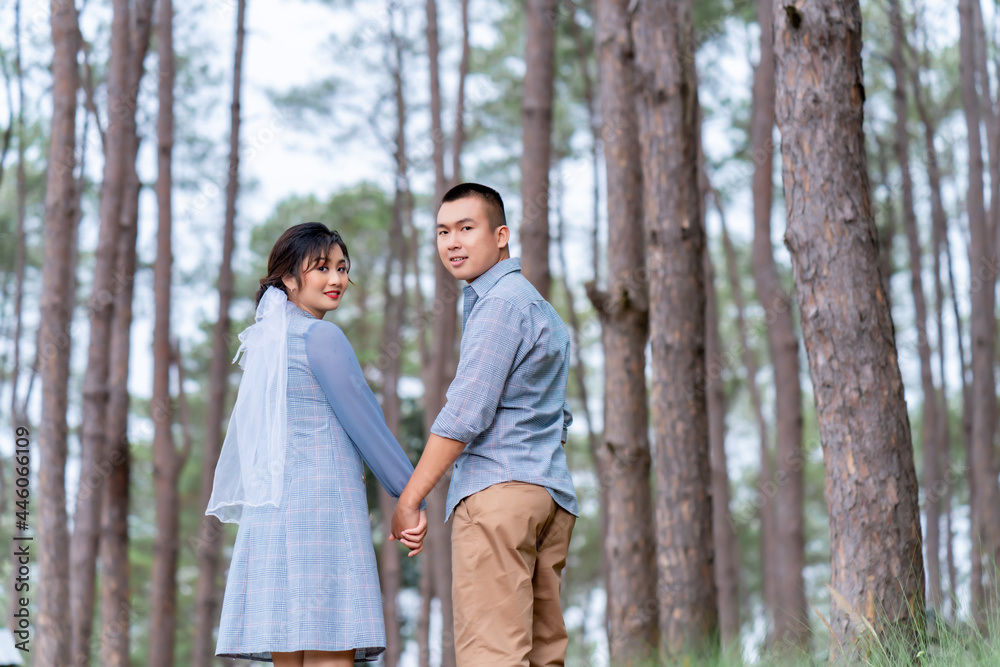 Portrait of an Asian couple posing for a pre-wedding photo in identical blue outfits, happily showing off their expressions of love in a pine garden.