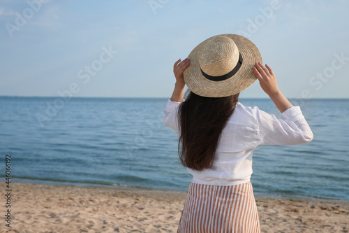Sticker Beautiful young woman wearing straw hat on beach, back view
