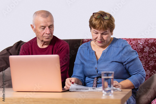 Aged couple going about their business, woman reading a newspaper and man opened laptop and sitting near his wife. photo