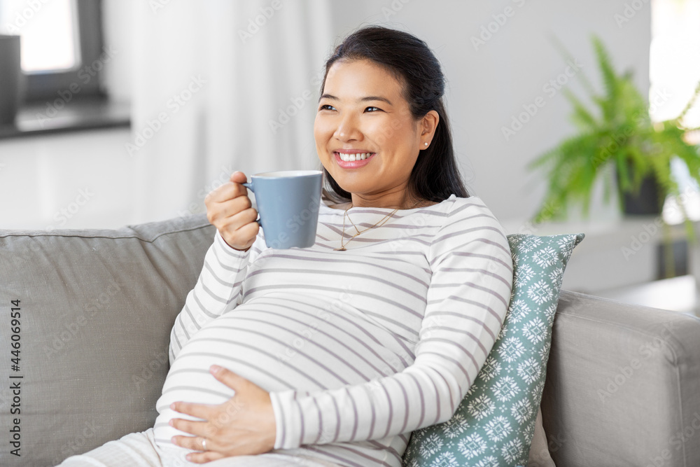 pregnancy, rest, people and expectation concept - happy smiling pregnant asian woman with mug sitting on sofa at home and drinking tea pregnancy, rest, people and expectation concept - happy smiling pregnant asian woman with mug sitting on sofa at home and drinking tea