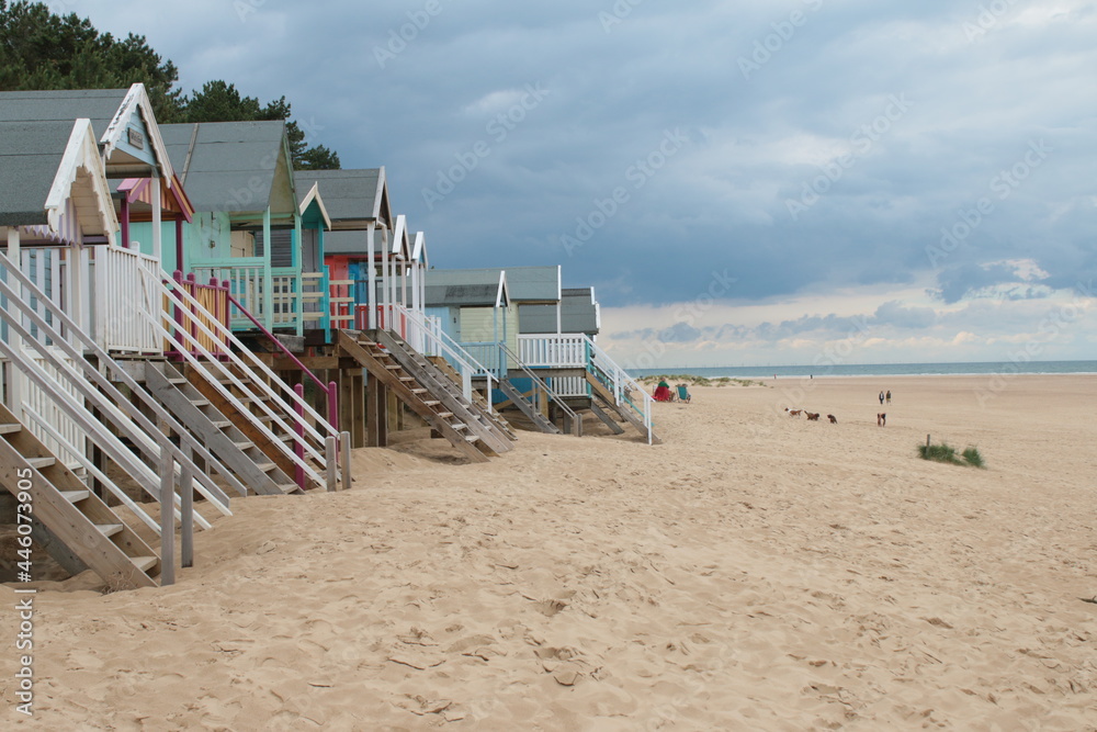 Landscape of beach huts on beautiful sandy beach coastline at Wells-Next-the-sea in Norfolk East Anglia on early Summer morning the sea on the horizon with painted wood huts foreground on holiday