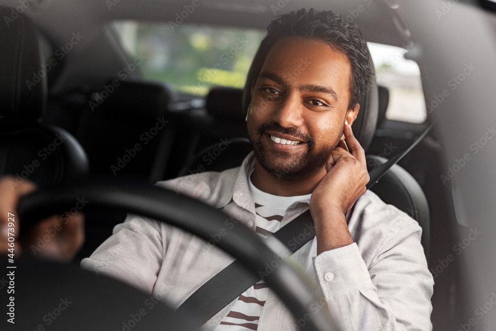 Obraz premium transport, people and technology concept - smiling indian man or driver with wireless earphones or hands free device driving car