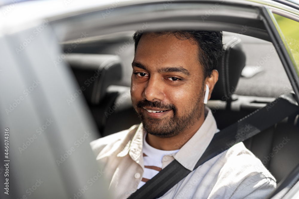 transport, people and technology concept - smiling indian man or driver with wireless earphones or hands free device driving car