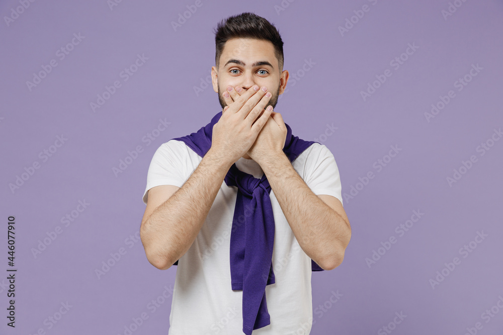 Attractive charming fun young brunet man 20s wears white t-shirt purple shirt look camera cover mouth with hand isolated on pastel violet background studio portrait. People emotions lifestyle concept
