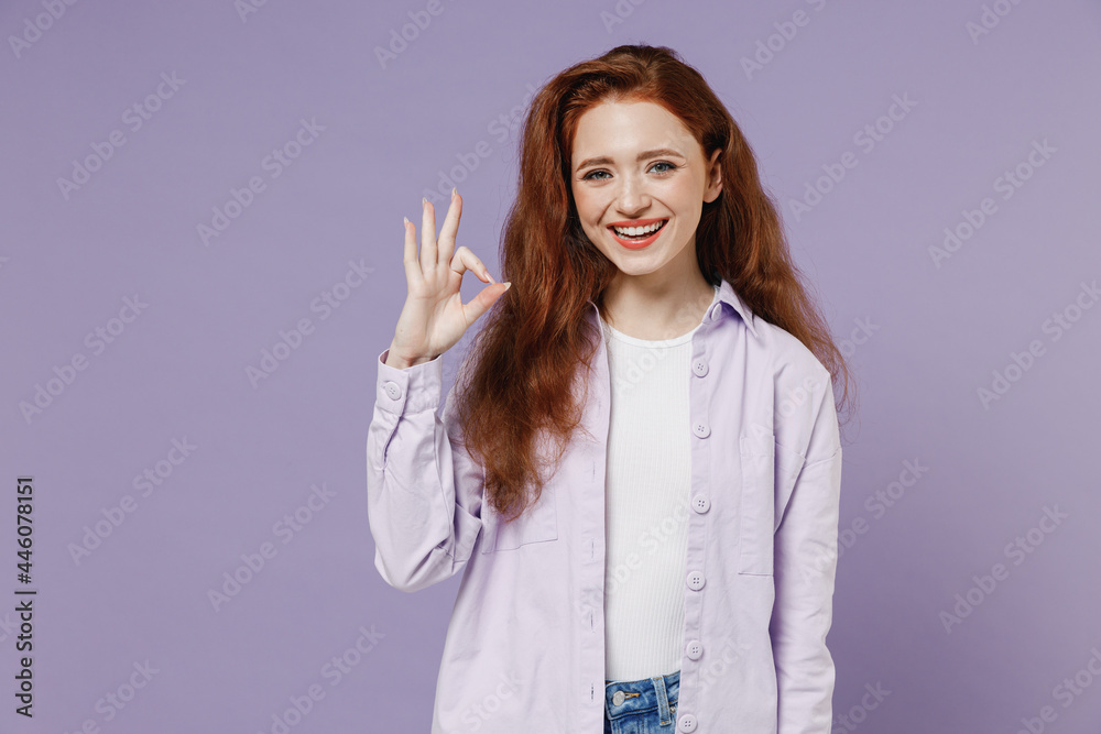 Smiling young redhead green-eyed woman 20s wears white T-shirt violet jacket showing okay ok gesture isolated on pastel purple color wall background studio portrait. People emotions lifestyle concept. Smiling young redhead green-eyed woman 20s wears white T-shirt violet jacket showing okay ok gesture isolated on pastel purple color wall background studio portrait. People emotions lifestyle concept.