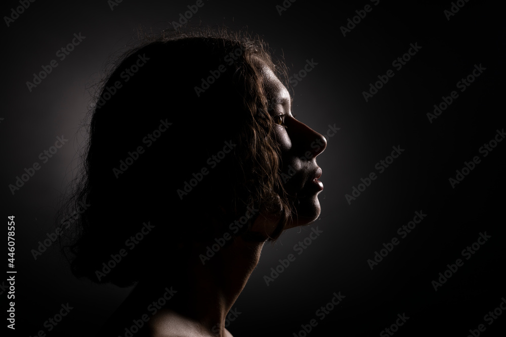 Portrait of a young woman in profile in the background light on a black background.
