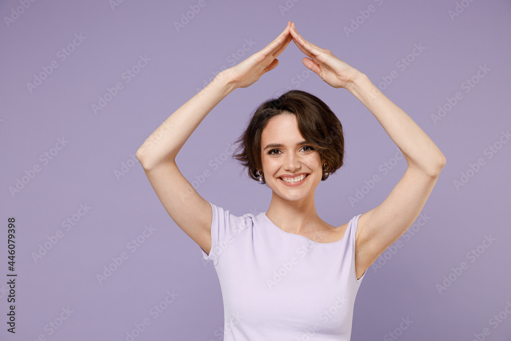 Young smiling happy woman 20s with bob haircut in white t-shirt hold folded hands above head like house roof, stay home isolated on pastel purple background studio portrait People lifestyle concept Young smiling happy woman 20s with bob haircut in white t-shirt hold folded hands above head like house roof, stay home isolated on pastel purple background studio portrait People lifestyle concept