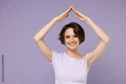 Young smiling happy woman 20s with bob haircut in white t-shirt hold folded hands above head like house roof, stay home isolated on pastel purple background studio portrait People lifestyle concept