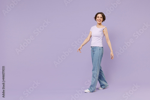 Full length side view young smiling happy woman 20s with bob haircut in white t-shirt looking camera walking going stroll isolated on pastel purple background studio portrait People lifestyle concept