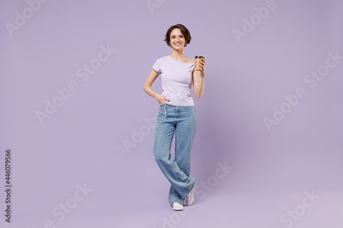 Full length young smiling satisfied fun happy woman 20s in white t-shirt hold takeaway delivery craft paper brown cup coffee to go stand akimbo isolated on pastel purple background studio portrait