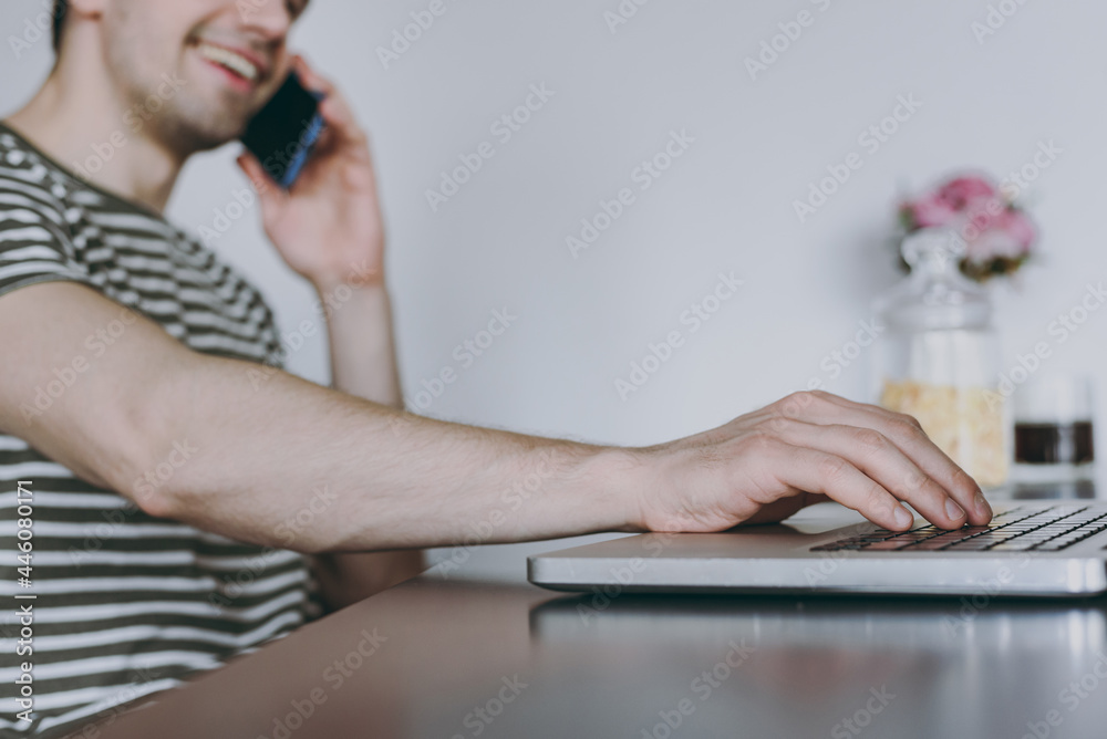 Fototapeta premium Cropped close up photo young man in t-shirt eat breakfast work online with laptop pc computer talk by mobile phone look for recipe cooking food in light kitchen at home alone People lifestyle concept