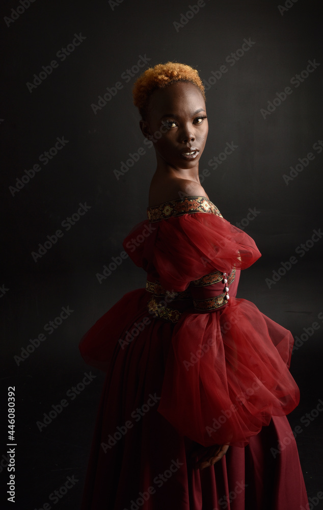 Classical  portrait of pretty African woman wearing red renaissance medieval fantasy gown,  shadowy lighting on a dark studio background.