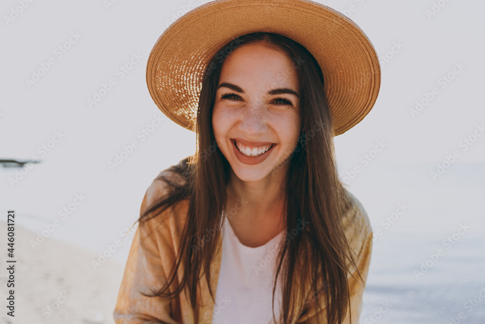 Close up laughing happy traveler tourist young woman 20s in straw hat shirt summer casual clothes standing look camera rest outdoorson sea beach background. People vacation lifestyle journey concept