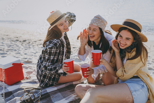 Three full size laughing friend young women in straw hat summer clothes have picnic hang out together drink liguor hold glasses together outdoor on sea beach background People vacation journey concept photo