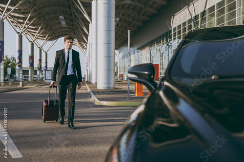 Full length young traveler businessman young man 20s wear black dinner suit going walk outside at international airport terminal with suitcase to car booking taxi. Air flight business trip concept © ViDi Studio