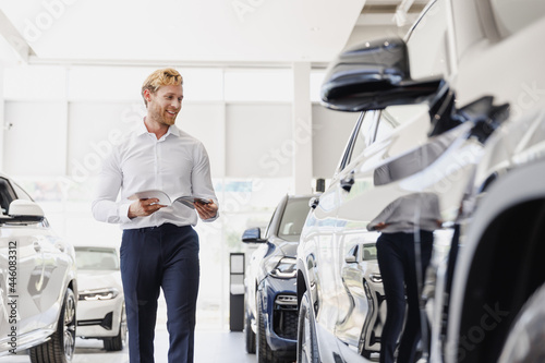Man satisfied customer male buyer client in white shirt read car papers documents agreement choose auto want buy new automobile in showroom vehicle dealership store motor show indoor Sales concept