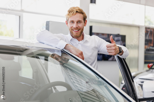 Fun man customer buyer businessman client in white shirt show thumb up get out car chooses auto want buy new automobile in showroom vehicle salon dealership store motor show indoor Car sales concept. © ViDi Studio