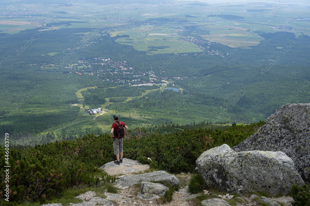 Rear view of an adult man looking at beautiful view in High Tatra mountains, Slovakia. Village Tatranska Lomnica, deep valley and forests seen from an elevated viewpoint